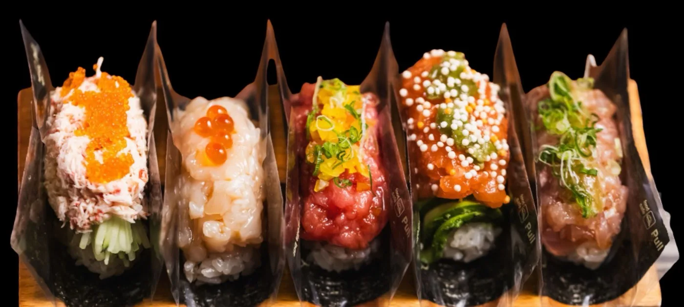 A row of made-to-order hand rolls on a wooden board